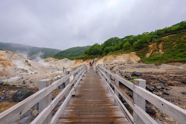 A timber boardwalk running out across the steaming crater floor of Jigokudani, Noboribetsu