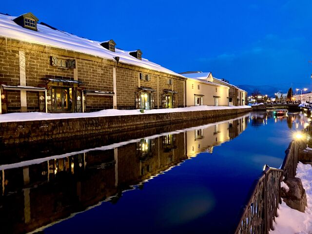 The Otaru canal at dusk in winter, snow on the warehouse roofs and lit windows reflected in still water