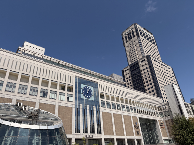 The south face of Sapporo Station with its round clock, the JR Tower rising behind it against a clear blue sky